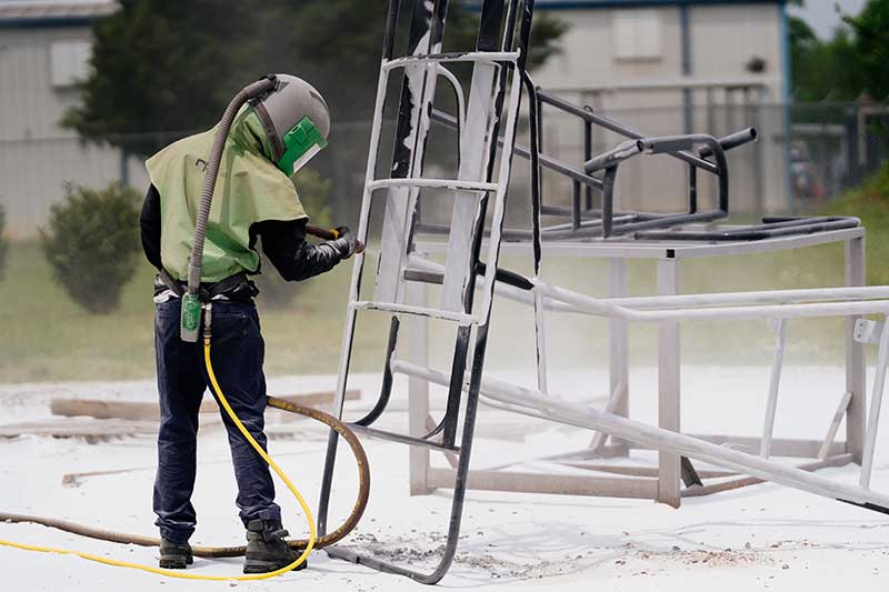 Tech wearing safety gear while spraying coating on metal bars outside.