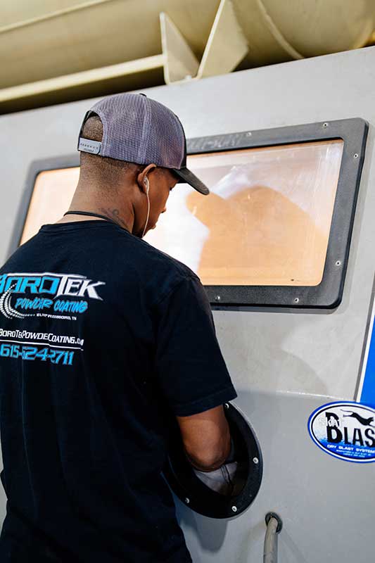 Tech operating sandblasting machine with a window to view progress.  He is wearing a BoroTek 5-shirt.