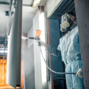 a person in protective gear and goggles powder coating a metal object