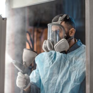 a person in protective gear (mask, gloves, etc.) spraying powder coating materials
