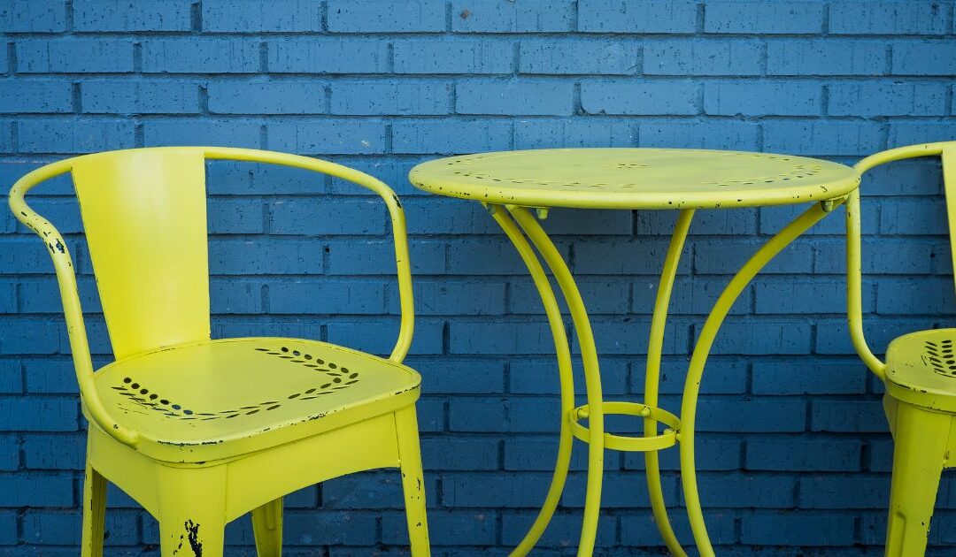 yellow metal chairs and table with chips and flaking paint against a blue brick wall